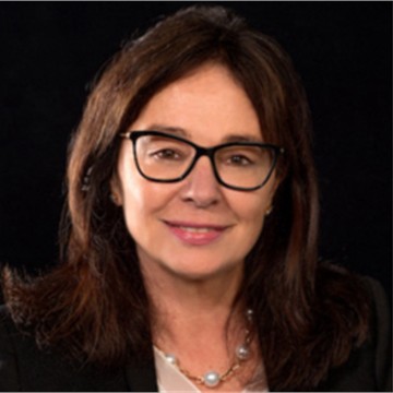 Professional headshot of a woman with brown hair and glasses wearing a pearl necklace against dark background
