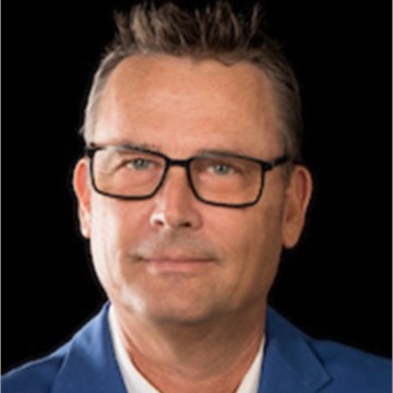 Professional headshot of a middle-aged man with glasses and short dark hair wearing a blue blazer against black background